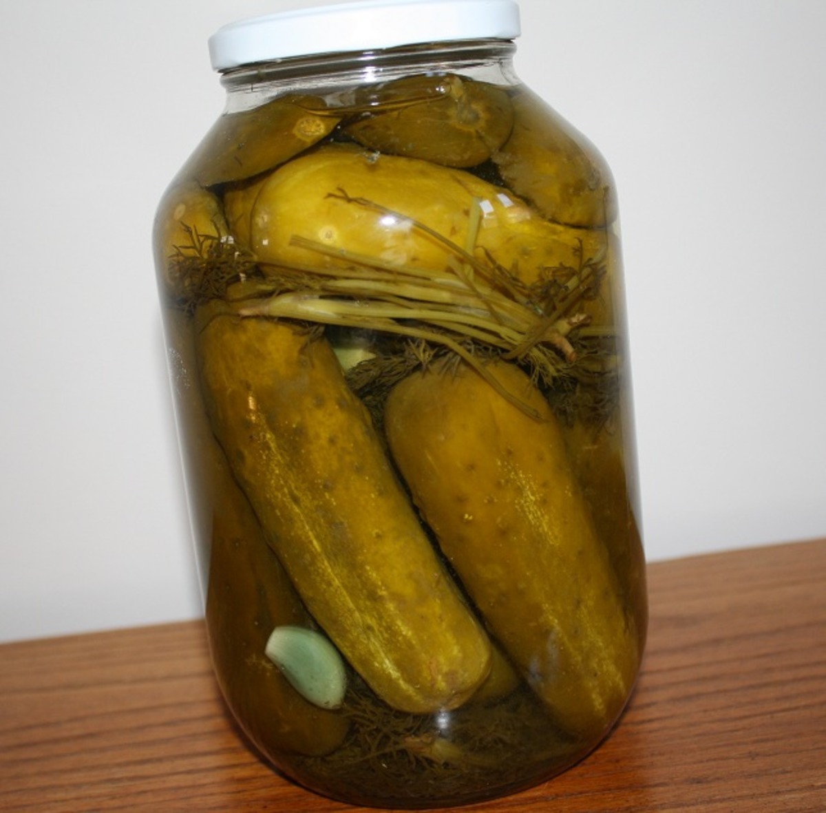 Phone photo of a large jar of home-pickled cucumbers on a table against a plain white wall
